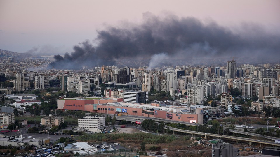a large cloud of smoke rises over a city at night