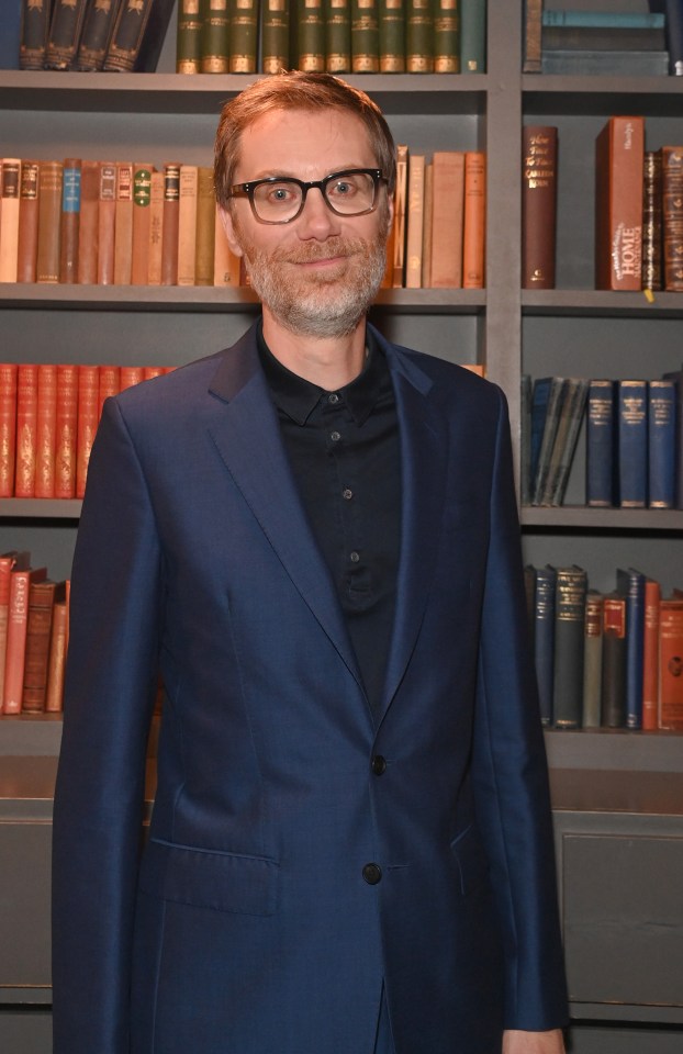 a man in a suit stands in front of a bookshelf with a book called home on it