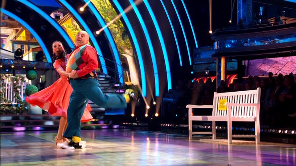 a man and a woman are dancing in front of a white bench with a yellow sign on it that says no entry