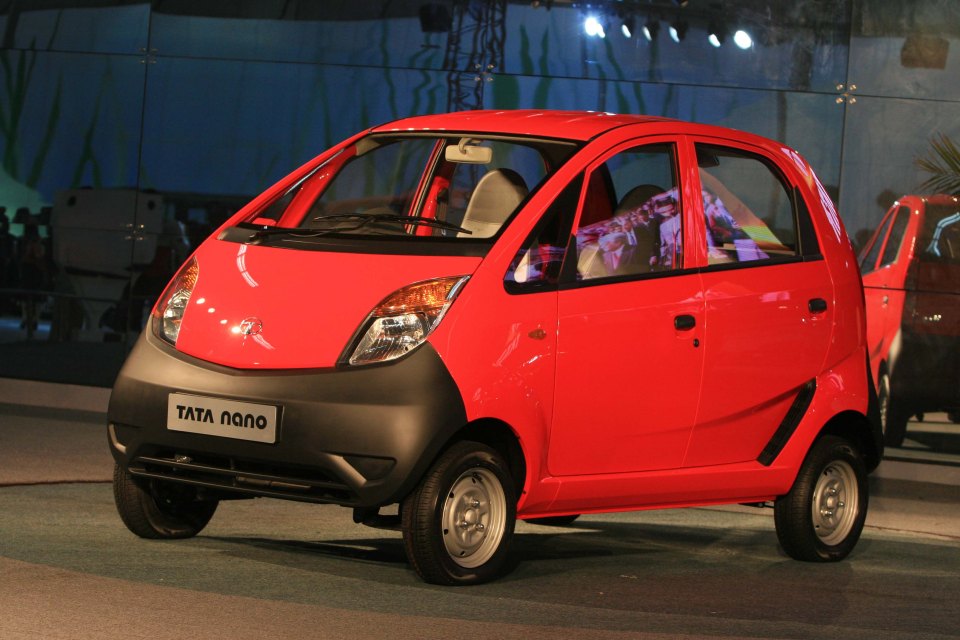 a red tata nano car is parked in front of a glass wall
