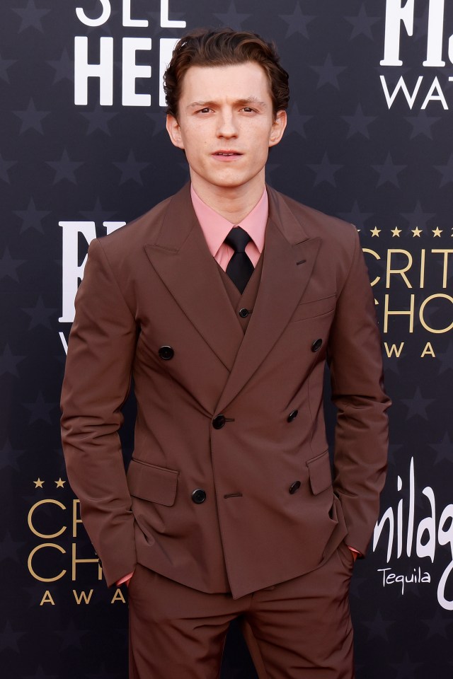 a man in a brown suit is standing on a red carpet that says critics choice awards