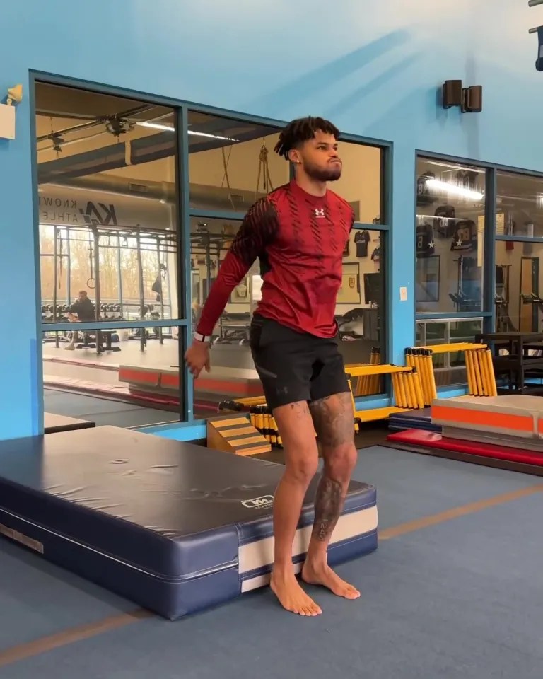 a man in a red under armour shirt is jumping on a mat in a gym