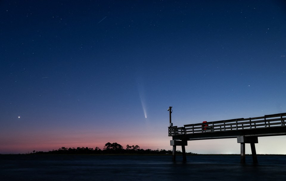 a person standing on a pier looking at a comet