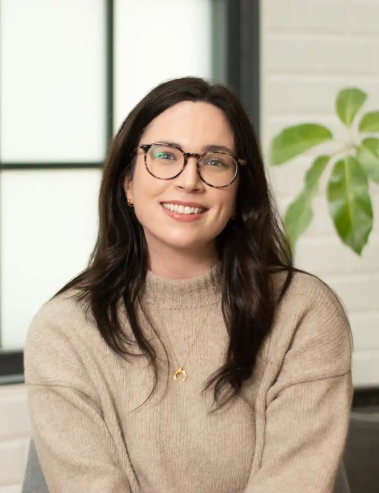a woman wearing glasses and a sweater is smiling for the camera .