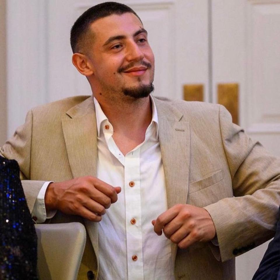 a man in a tan suit and white shirt is smiling