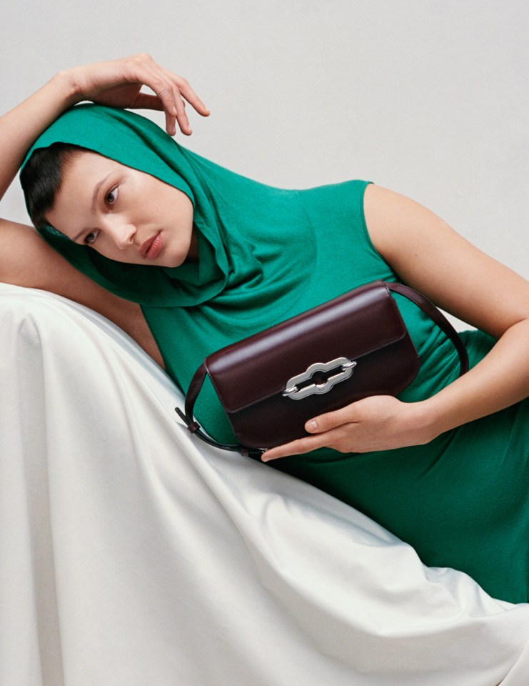 a woman in a green dress is laying on a couch holding a brown bag
