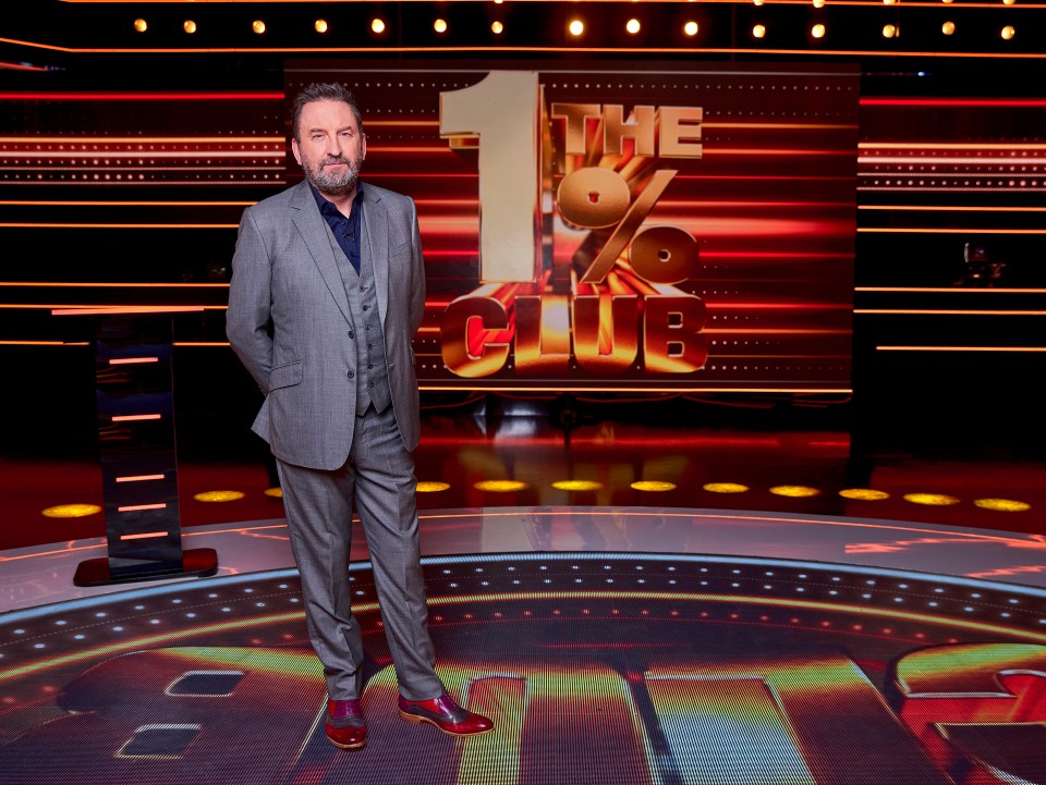 a man in a suit stands in front of a sign that says the 1 % club