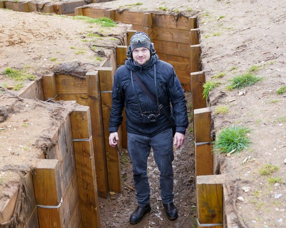 a man wearing a helmet and goggles stands in a wooden trench
