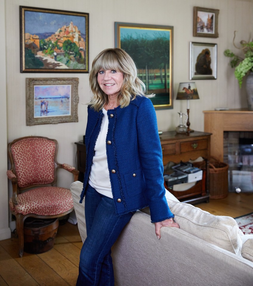 a woman in a blue jacket leans on a couch in a living room