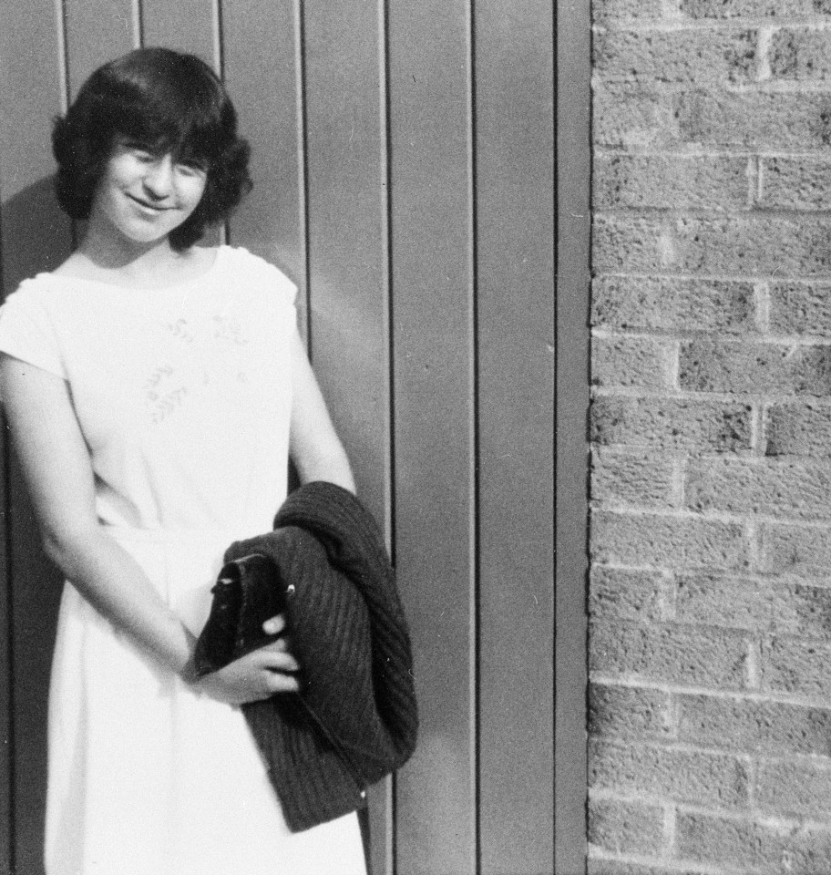 a woman in a white dress stands in front of a brick wall
