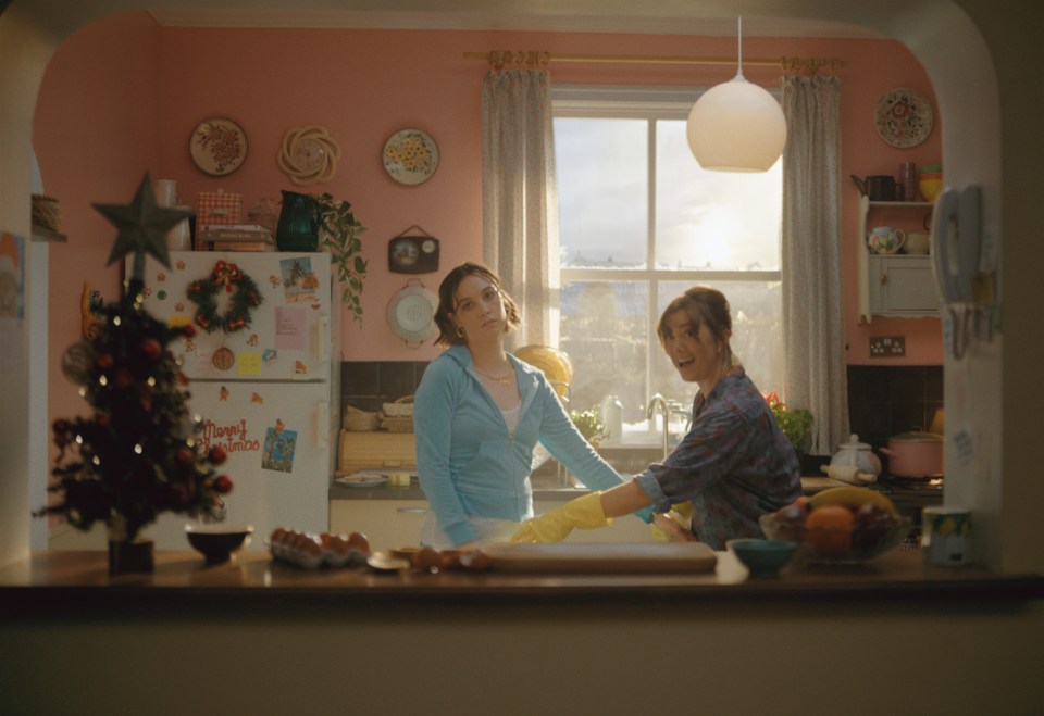 two women standing in front of a refrigerator that has a christmas wreath on it