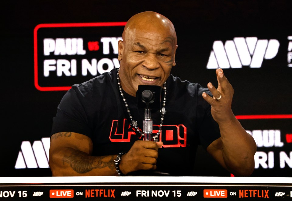 mike tyson speaking into a microphone in front of a paul vs ty friday sign