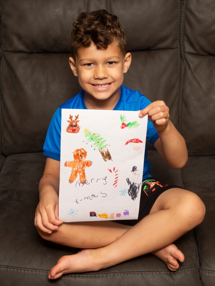 a young boy is sitting on a couch holding a drawing that says merry xmas