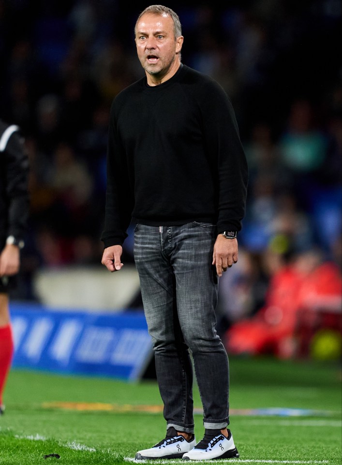 a man in a black sweater and jeans stands on a soccer field