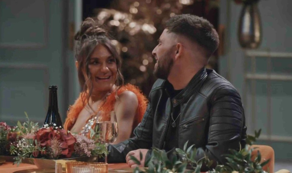 a man in a leather jacket sits next to a woman at a table