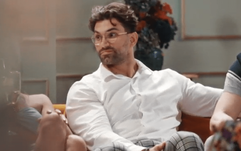a man wearing glasses and a white shirt is sitting on a couch .