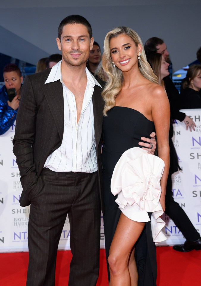 a man in a suit and a woman in a black dress pose on a red carpet