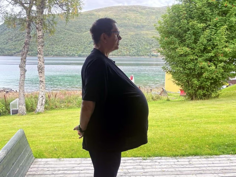 a man in a black shirt stands in front of a lake