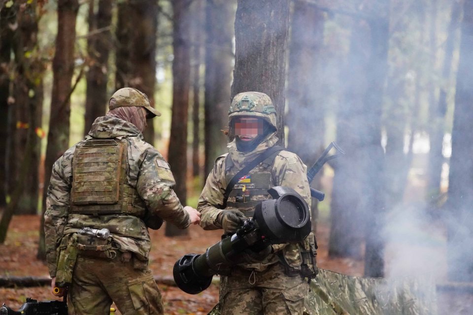 two soldiers are talking in the woods with one holding a rocket launcher