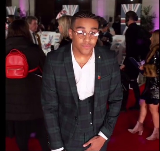 a man in a suit and glasses stands on a red carpet