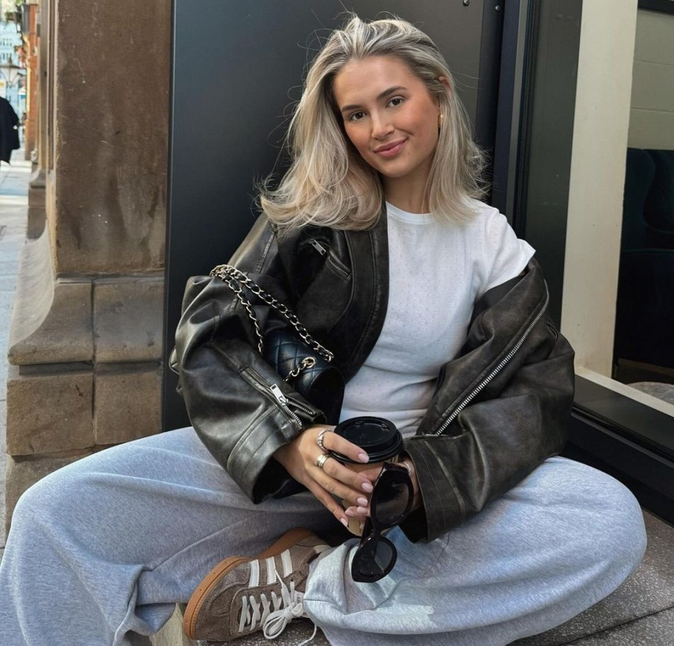 a woman in a leather jacket sits on the sidewalk holding a cup of coffee