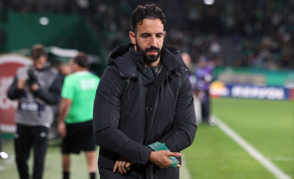 a man in a black jacket stands on a soccer field
