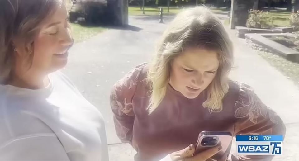 two women are looking at a cell phone and the time is 6:16