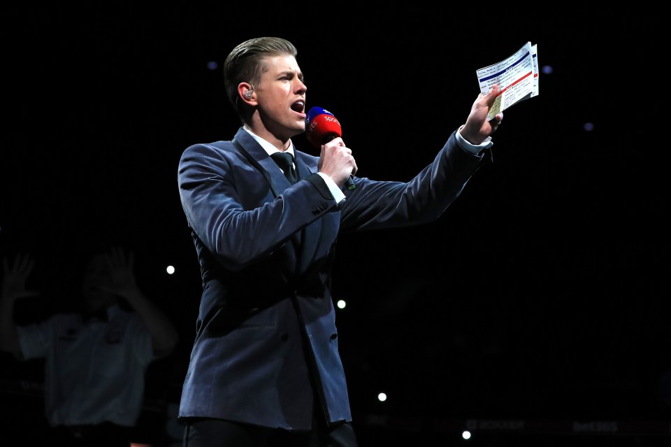 a man in a suit is holding a red microphone and a piece of paper