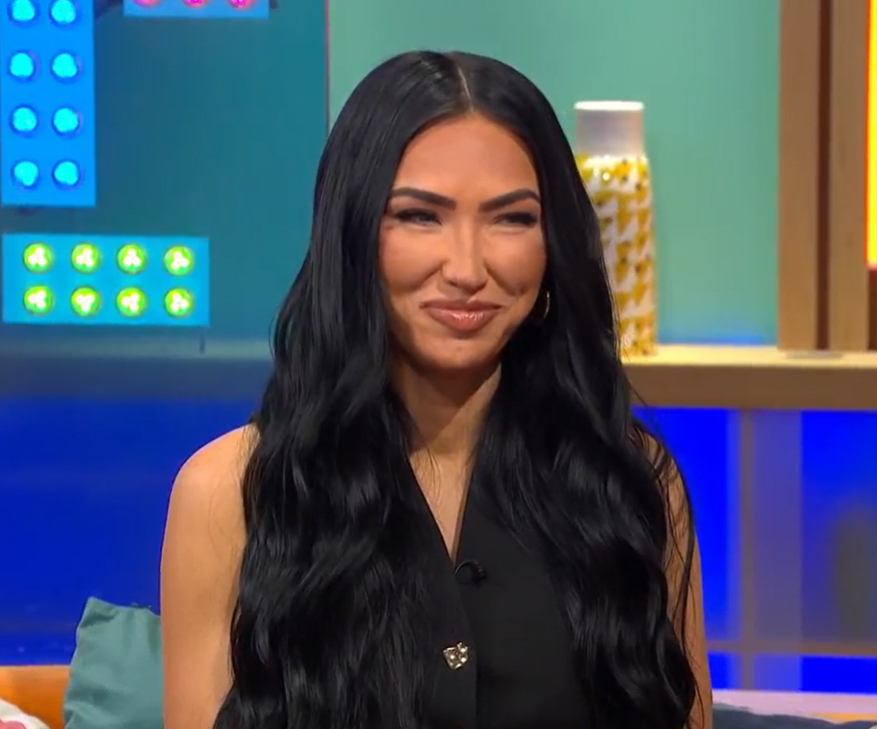 Woman with long black hair smiling on a talk show.