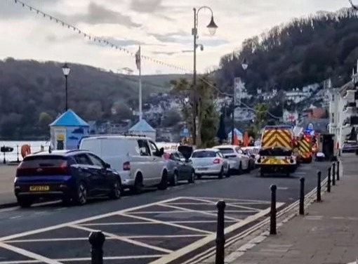 a row of cars are parked on the side of a street next to a body of water .