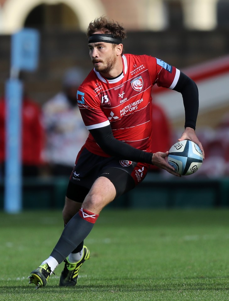 a man in a red mitsubishi motors jersey runs with a rugby ball