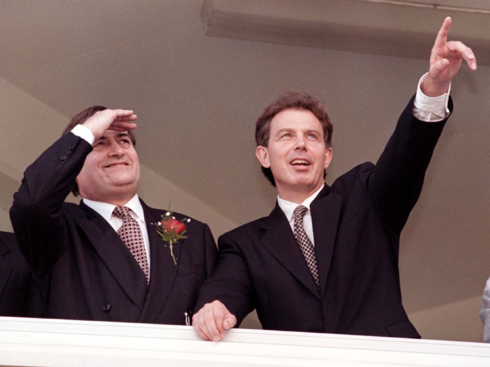 two men in suits are standing next to each other and one is pointing up