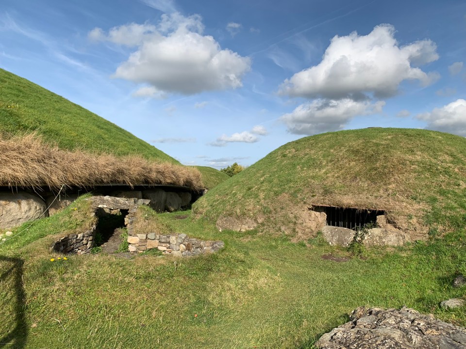 two grassy hills with a blue sky and clouds behind them