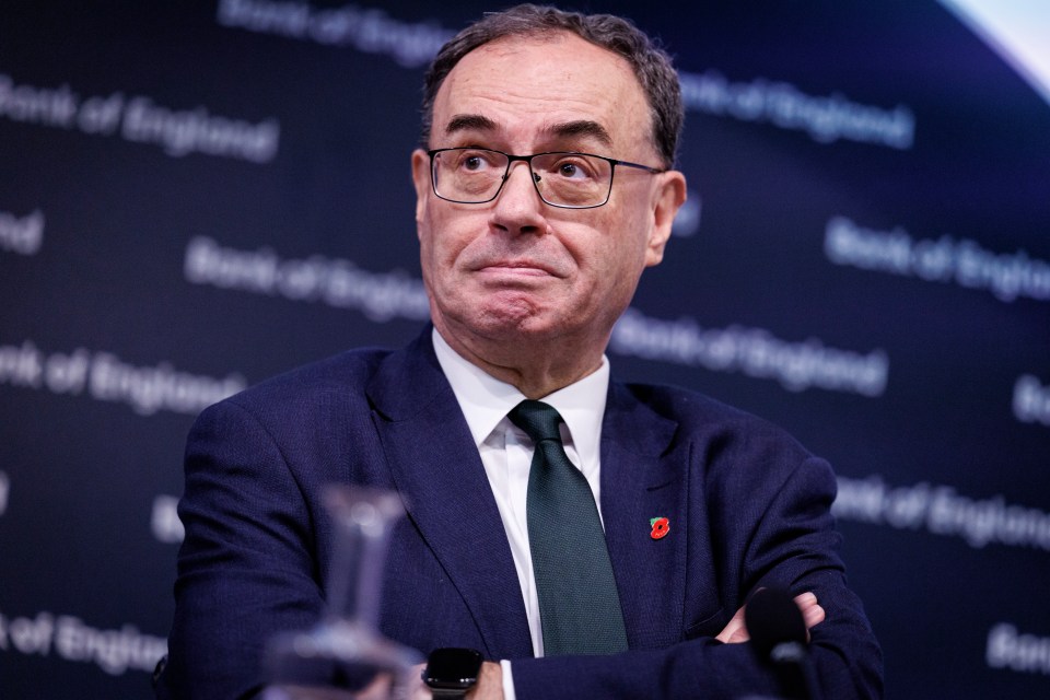 a man in a suit and tie stands in front of a wall that says bank of england