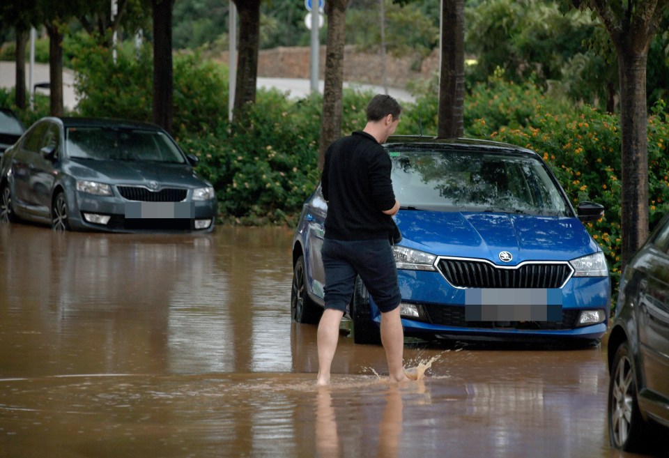 a man stands in a flooded parking lot next to a blue skoda car