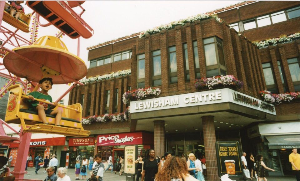 a boy rides a ferris wheel in front of the lewisham centre