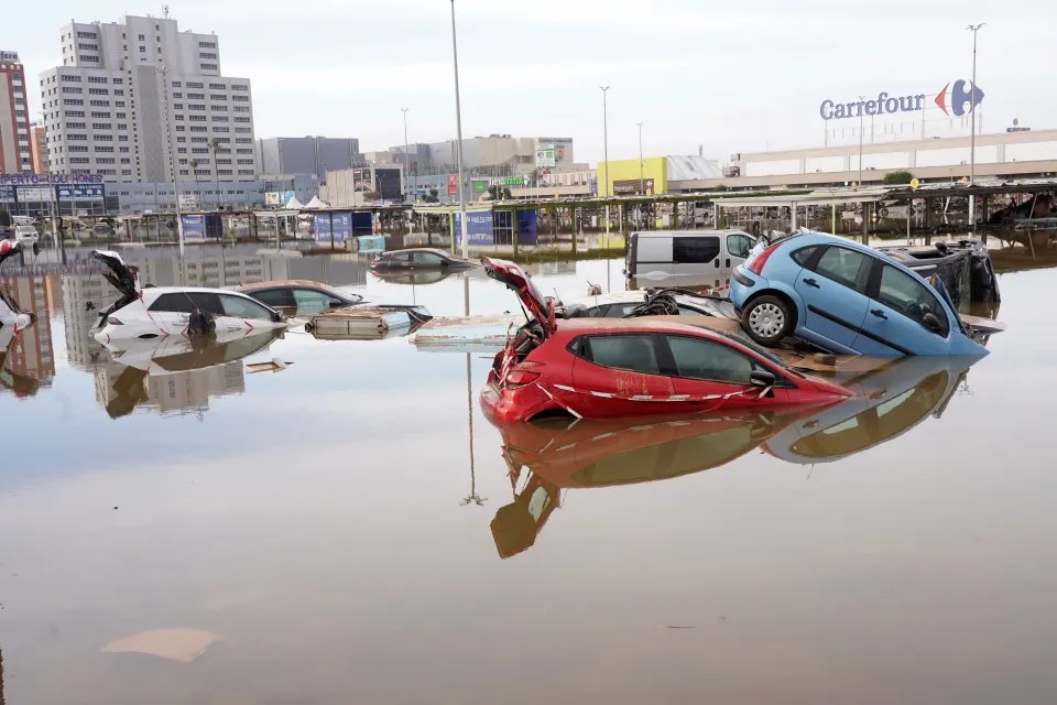 cars are floating in a flooded parking lot in front of a carrefour store
