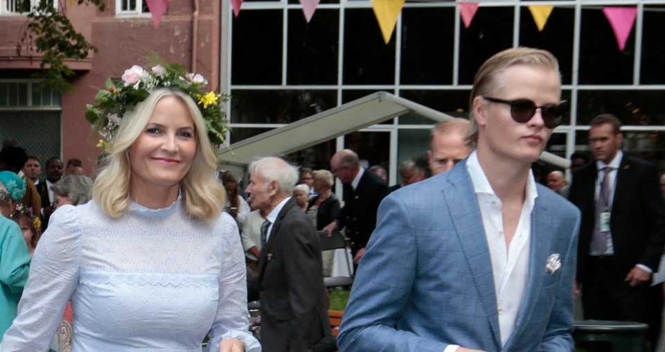 A woman wearing a flower crown and a light blue dress walks alongside a young man in a light blue suit.