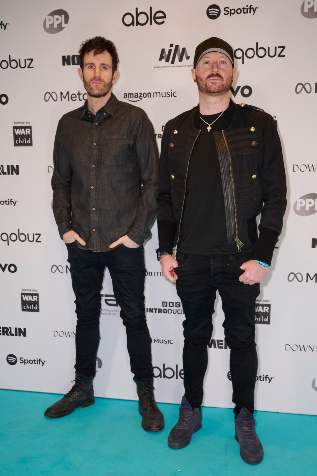 two men stand on a blue carpet in front of a wall that says able