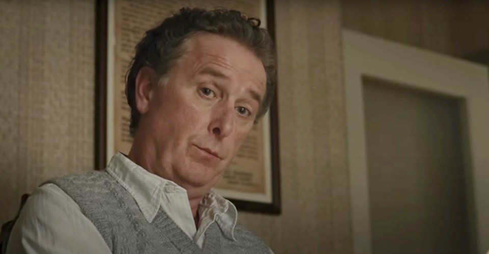 a man wearing a grey vest and white shirt looks at the camera
