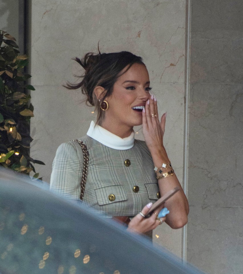 a woman covering her mouth with her hand while holding a cell phone