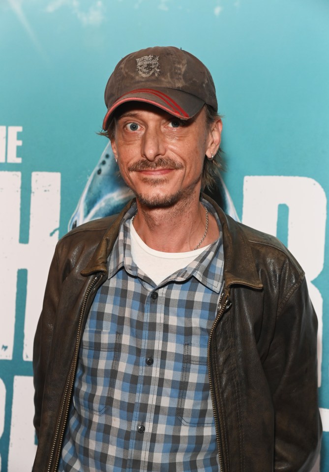 a man wearing a hat and a plaid shirt stands in front of a sign that says the shark