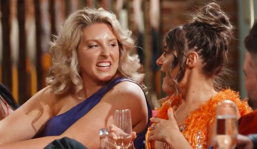 two women are sitting at a table with glasses of wine