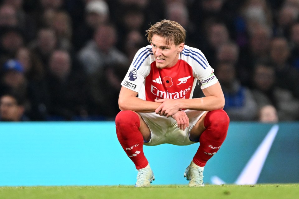 a soccer player wearing a red emirates jersey squats on the field