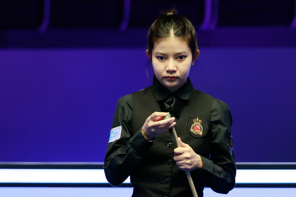 a woman is holding a pool cue and wearing a black vest with a crown on it