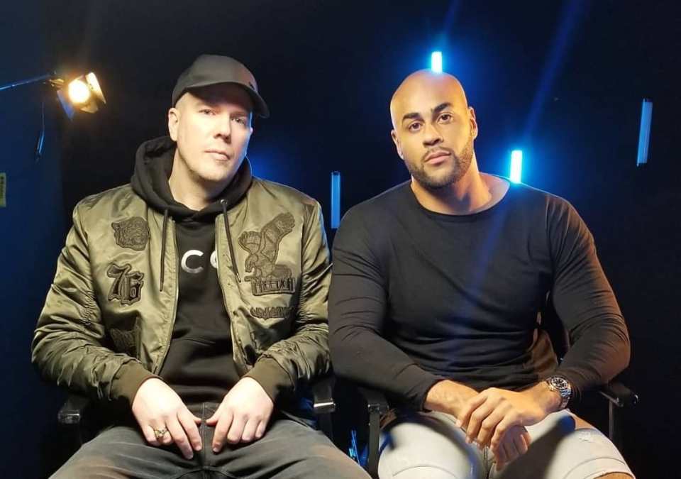 two men sitting next to each other with one wearing a jacket with the letter c on it