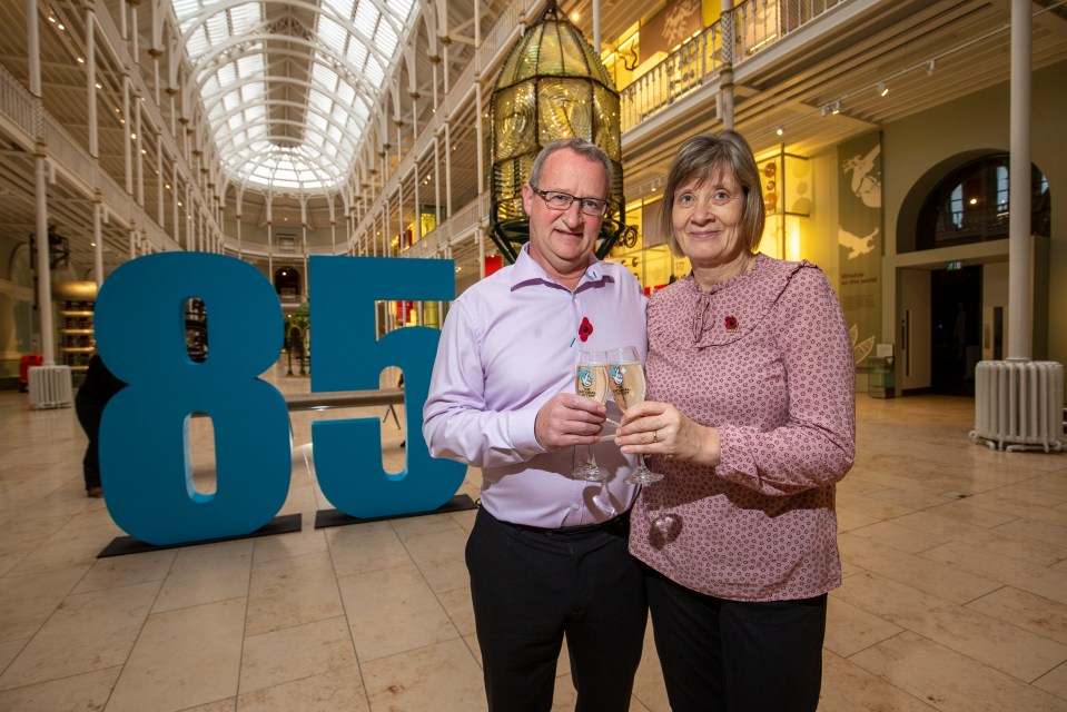 a man and woman stand in front of a large blue number 85