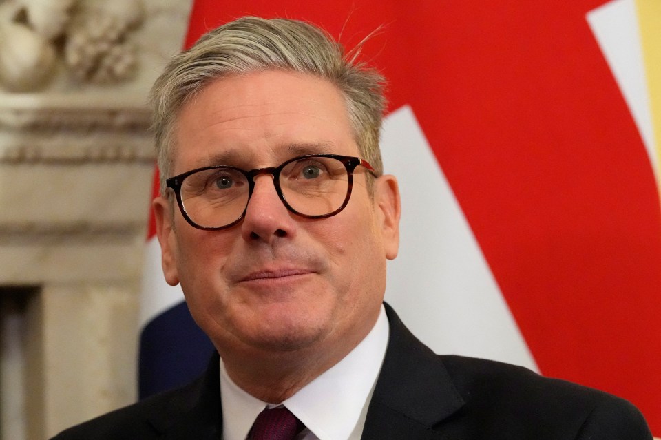 a man wearing glasses and a suit stands in front of a red and white flag