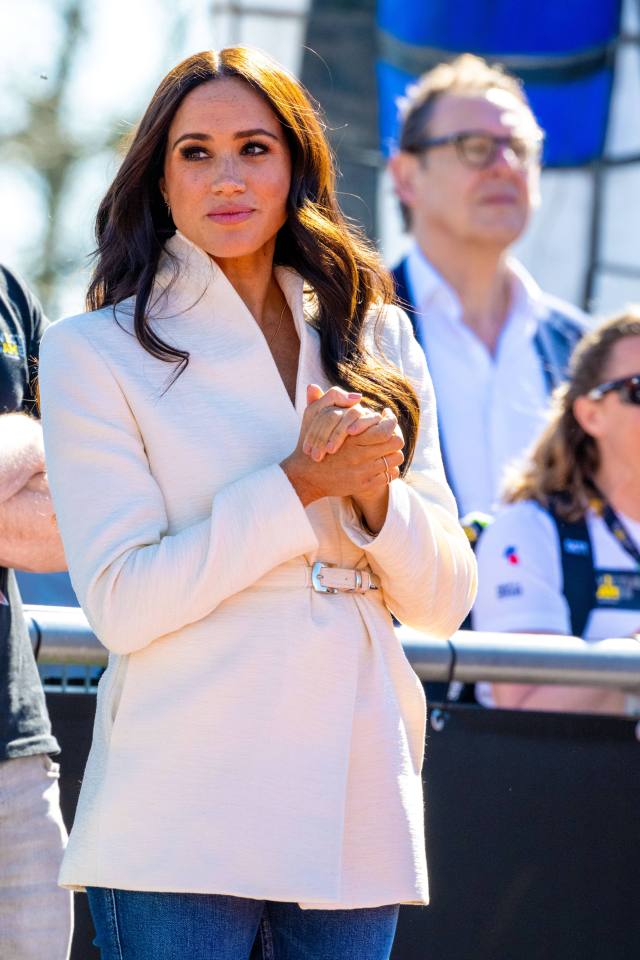 a woman in a white jacket stands with her hands folded
