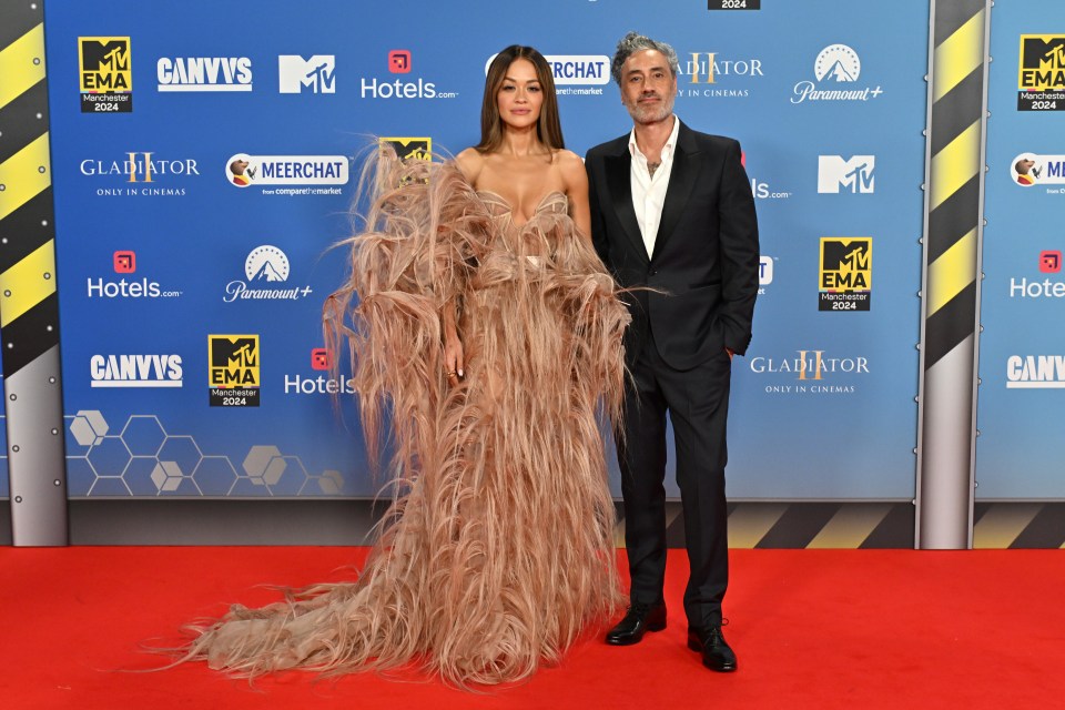 a woman in a feathered dress and a man in a suit pose on a red carpet for mtv ema awards